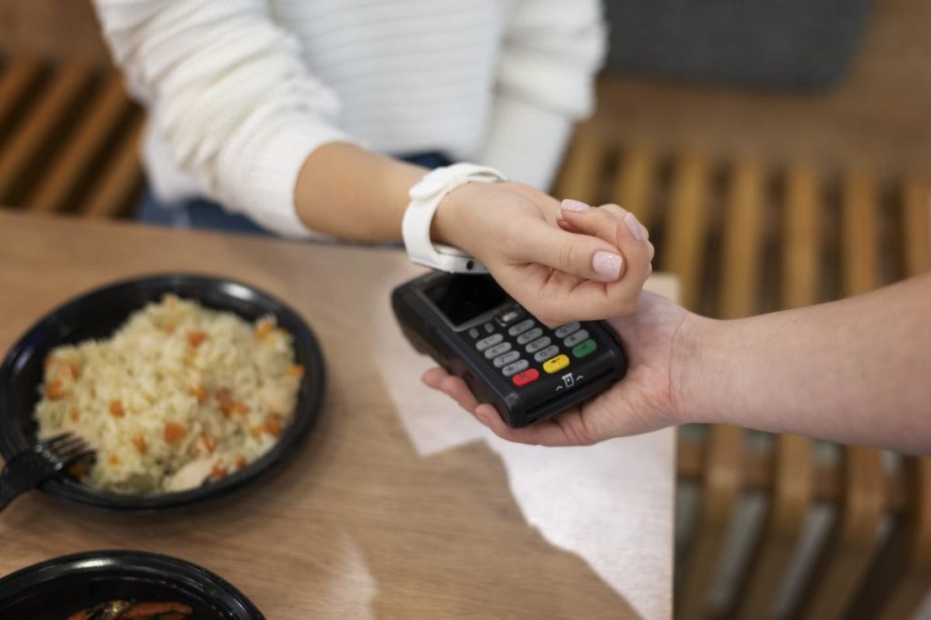 mulher com smartwatch branco colocando ele em cima de uma máquina de cartão para efetuar o pagamento em um restaurante