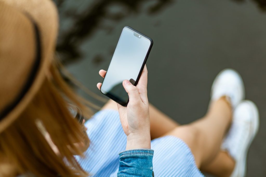 mulher de chapéu, sentada usando o celular com uma mão apenas