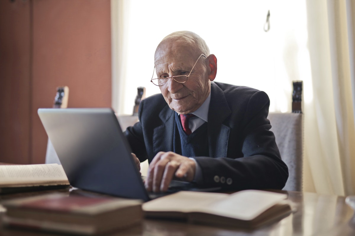 Um senhor idoso usando um computador, vestido com terno e gravata