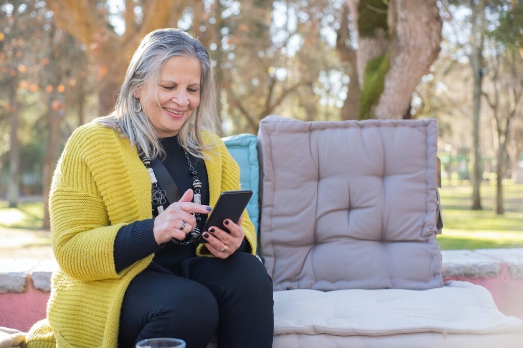 Lensa: Idosa usando um smartphone em uma praça pública.