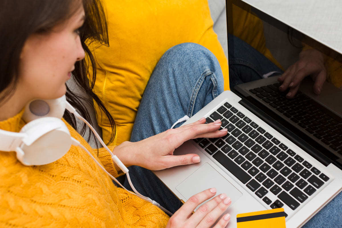 Mulher sentada com notebook no colo e fone de ouvido ao redor do pescoço