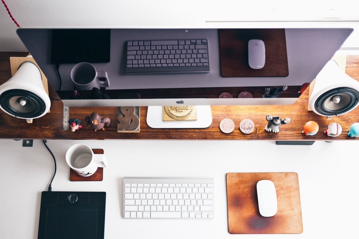 Computador sobre mesa de madeira com teclado pequeno e ao lado de outros itens de escrivaninha