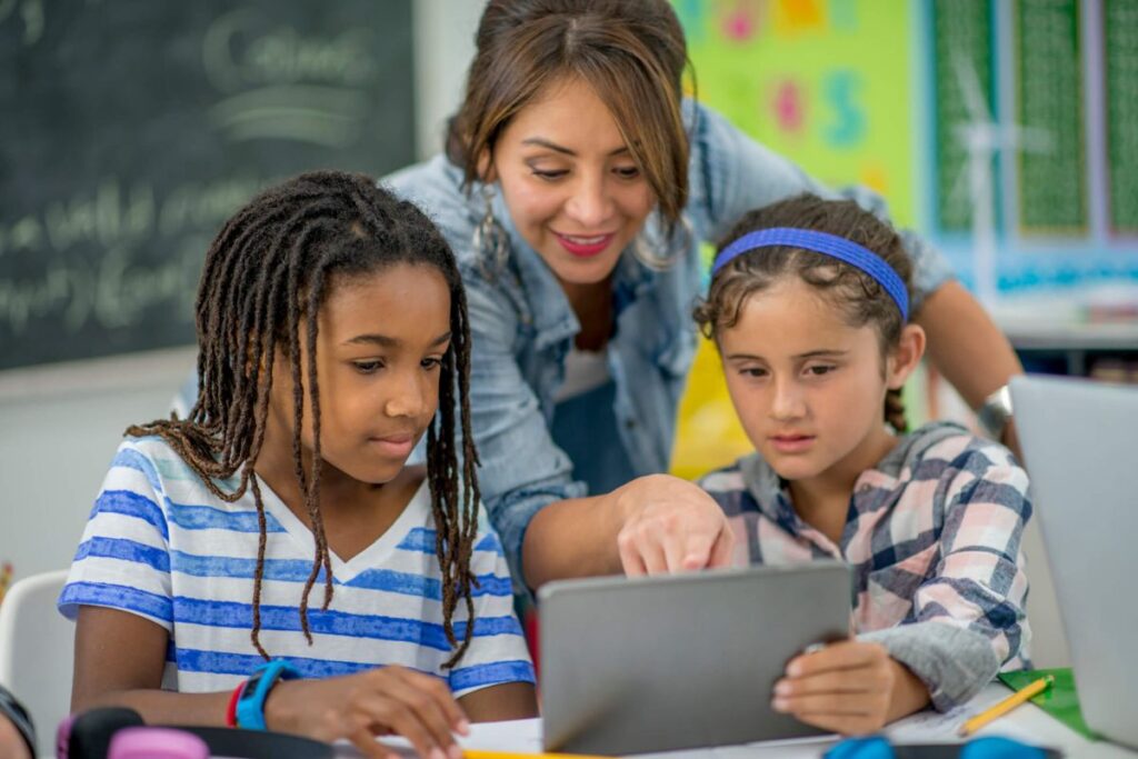 educação: a imagem mostra uma professora mostrando algo em um tablet para os alunos 