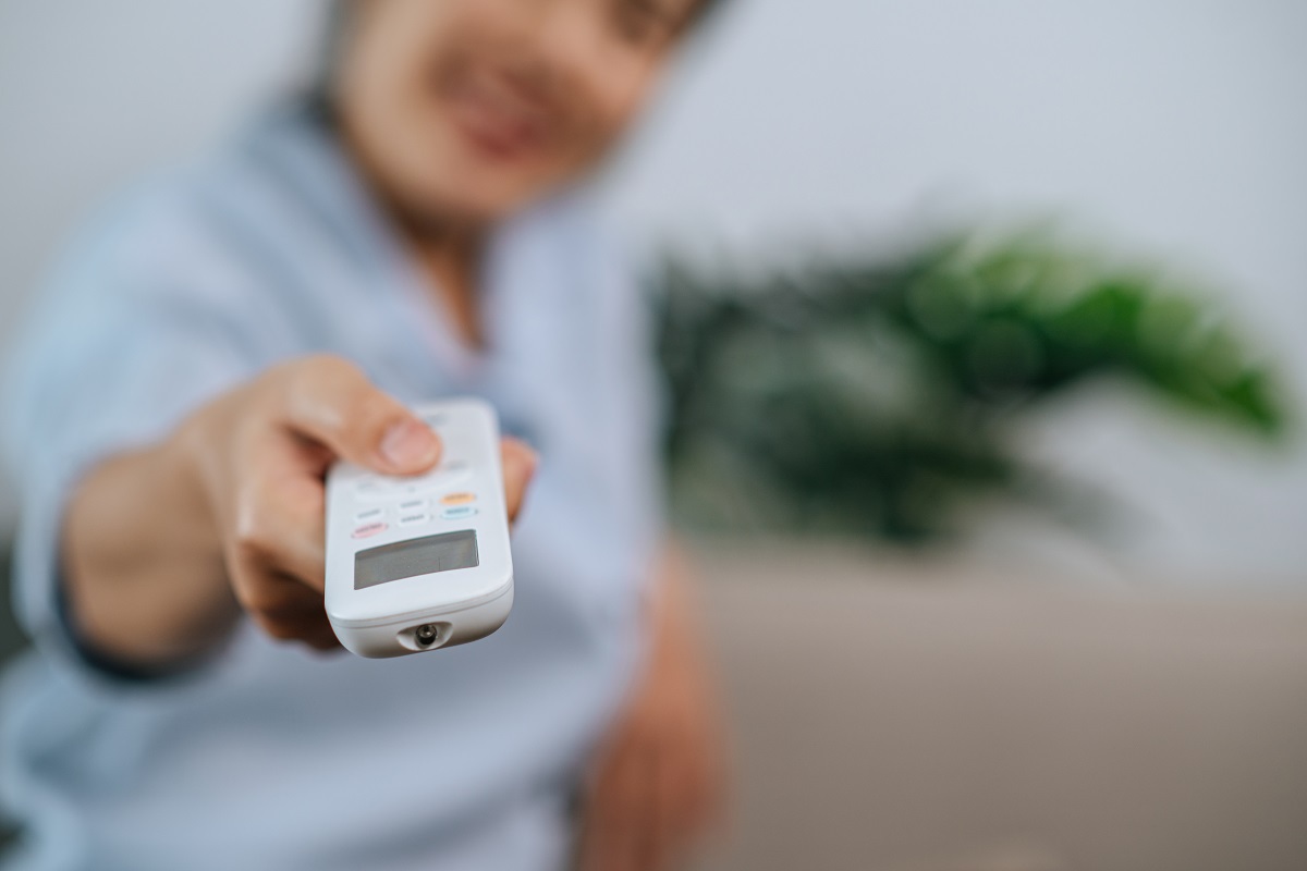 Pessoa apontando controle remoto para aparelho que não aparece na foto