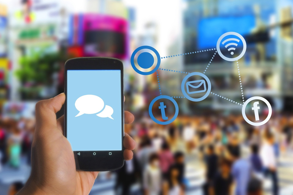 Mão de usuário com celular na mão com sua tela mostrando símbolo de sms ou bate papo e ao lado símbolos web diversos representando a Tecnologia social