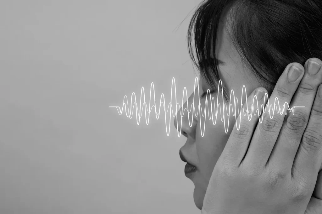 Mulher com as mãos nos ouvidos e ondas sonoras representadas graficamente à sua frente, simbolizando audição e processamento de som.