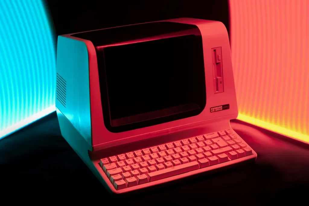 Computador vintage IBM com teclado e tela, iluminado por luzes neon vermelhas e azuis.