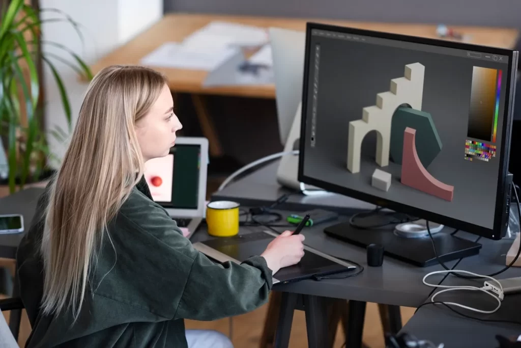 Designer digital utilizando uma mesa digitalizadora para desenvolver formas geométricas em software de modelagem 3D exibido na tela do computador.